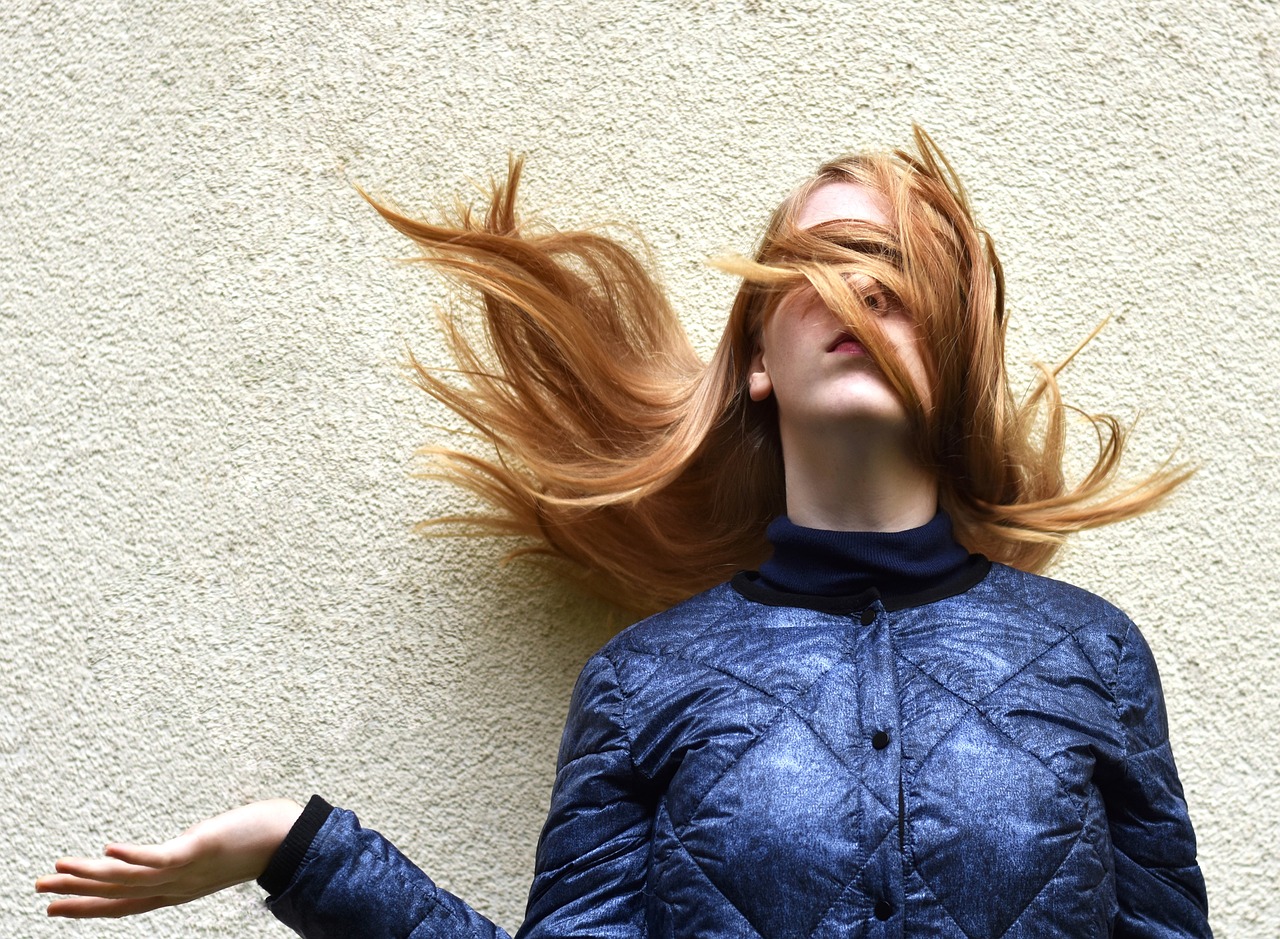 A woman with red hair blown over her face and eyes.