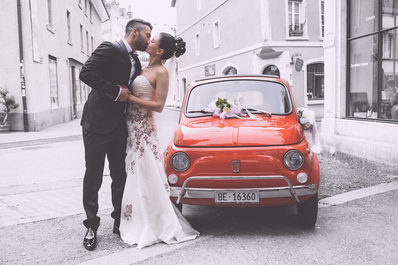 Bride and groom standing by a car.